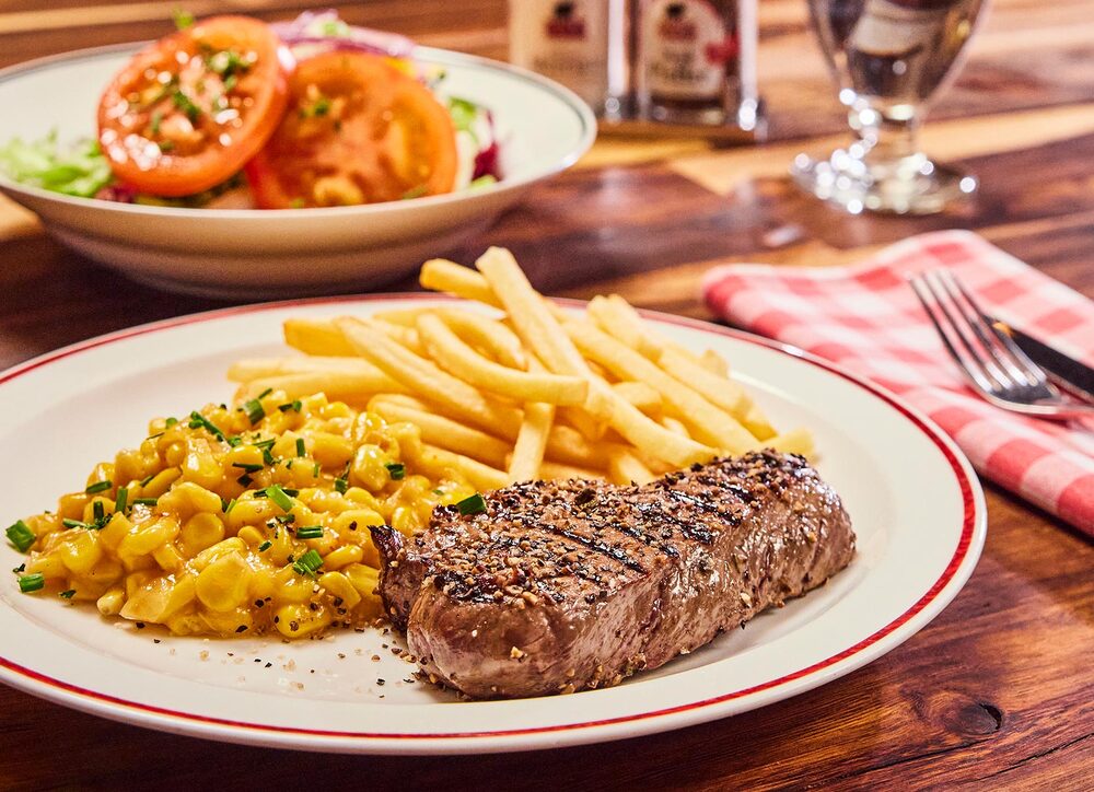 Mittagstisch im BLOCK HOUSE Steakrestaurant Huftsteak mit Pommes und Maisgemüse auf einem Teller serviert, dazu ein Salat