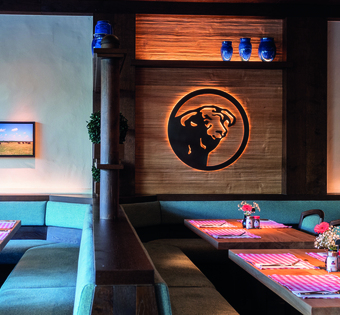 Köln Innenraum des BLOCK HOUSE Restaurants in Köln; mehrere Tischreihen mit Platzsets, Gewürzen und Blumen; das BLOCK HOUSE Bullenlogo wird an einer Holzwand von hinten erleuchtet