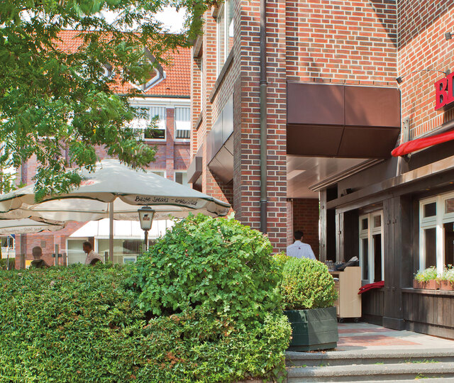 Hamburg Eidelstedt Außenfassade des BLOCK HOUSE Restaurants Eidelstedt in Hamburg. Links im Bild ist die Terrasse mit grüner Umrandung und Sonnenschirmen zu sehen.