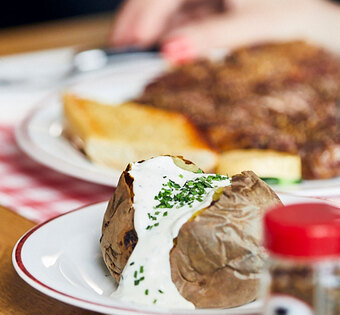 Essen Blick auf einen gedeckten Tisch im BLOCK HOUSE: Ein Glas Wasser, eine Baked Potato mit Sour Cream, Gewürze und im Hintergrund ein Steakteller