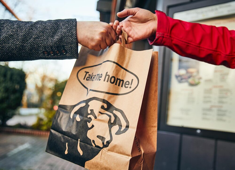 Click & Collect: Steakhouse-Genuss für zu Hause BLOCK HOUSE Mitarbeiter übergibt eine Takeaway Papiertüte mit der Aufschrift „Take me home!“