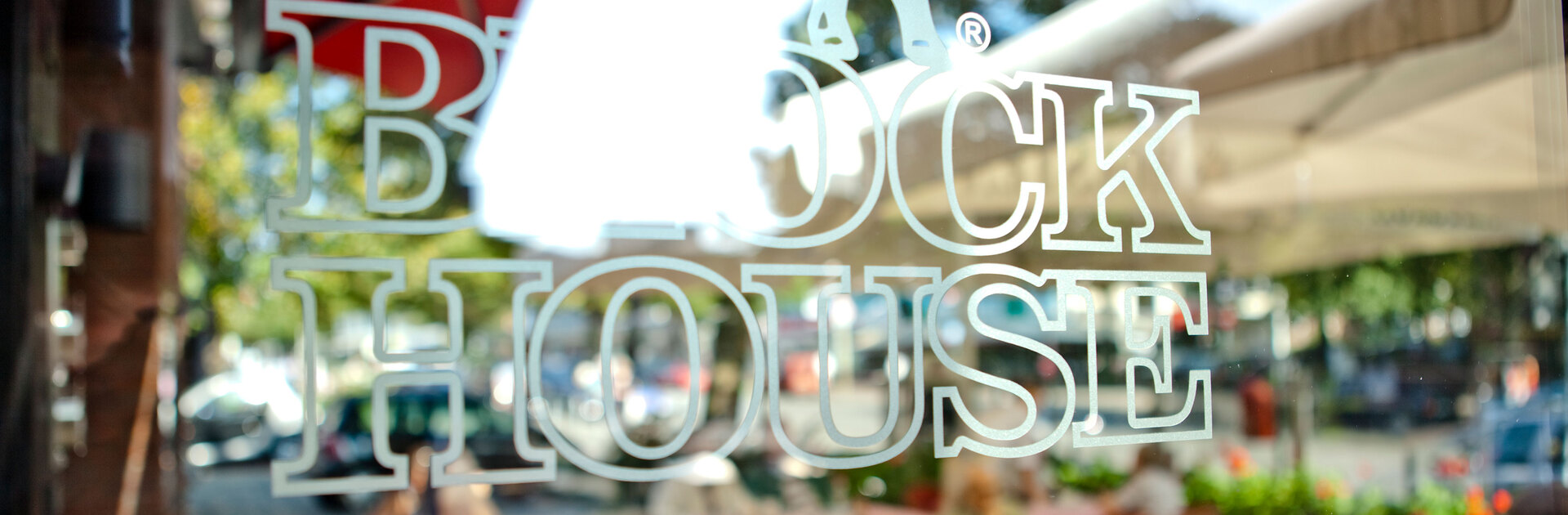 Hamburg Barmbek Blick auf den Schriftzug BLOCK HOUSE auf einer Glasscheibe. Im Hintergrund ist die Terasse des BLOCK HOUSE Restaurants Barmbek zu sehen.