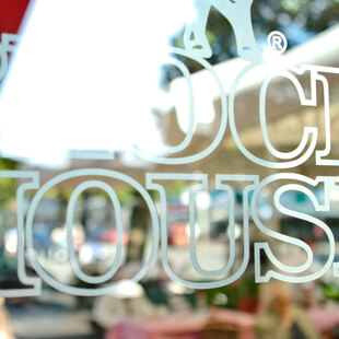 Hamburg Barmbek Blick auf den Schriftzug BLOCK HOUSE auf einer Glasscheibe. Im Hintergrund ist die Terasse des BLOCK HOUSE Restaurants Barmbek zu sehen.