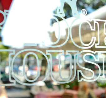 Hamburg Barmbek Blick auf den Schriftzug BLOCK HOUSE auf einer Glasscheibe. Im Hintergrund ist die Terasse des BLOCK HOUSE Restaurants Barmbek zu sehen.